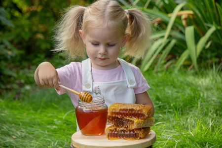 Little Girl Eating Honey with Honeycomb Outdoors.の写真素材