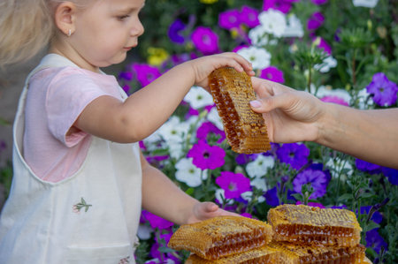 Little Girl Eating Honey with Honeycomb Outdoors.の写真素材