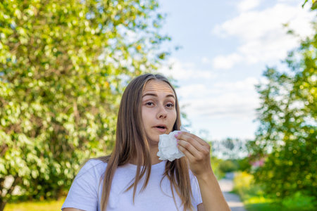 Woman holding a tissue to her nose, appearing to sneeze.の写真素材