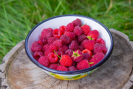Raspberries in a bowl on a stump in the garden.