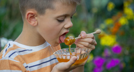 Boy eating honey on a garden background. Selective focus.