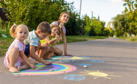 Children draw a picture with chalk on the asphalt. A rainbow, house, sun, clouds are drawn on the...