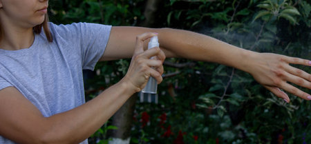 Woman applying insect repellent spray on her hand. Concept of preventing mosquito bites.