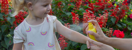 Father insect applying repellent spray to child's hand outdoors. Selective focus.