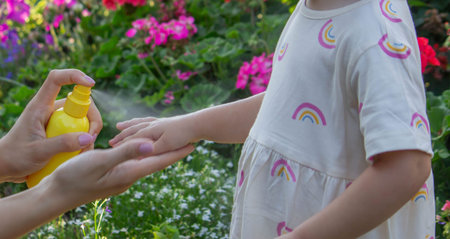 Father insect applying repellent spray to child's hand outdoors. Selective focus.