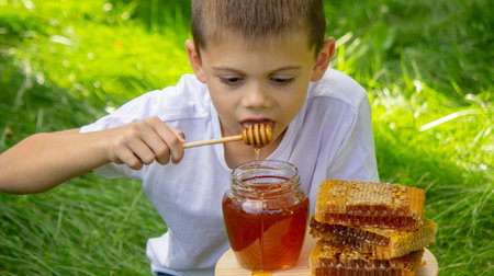 Boy eating honey on the background of the garden. Selective focus.