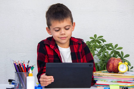 Boy studying remotely. Boy studying with books and his digital tablet at home.