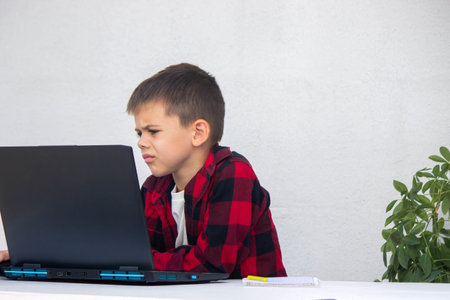 Schoolboy studying online on laptop at home, sitting at table. Distance learning