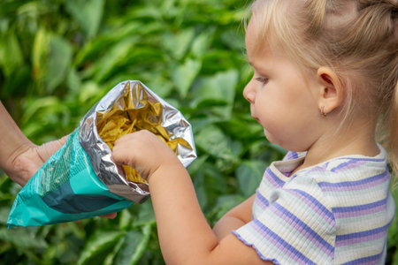 Girl with a pack of chips on a nature background. Unhealthy eating.