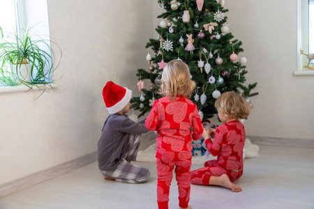 Three children in pajamas decorating a Christmas tree. Christmas Tradition.の写真素材