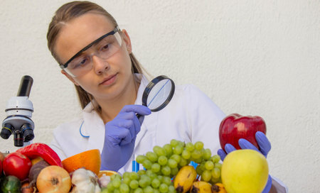 Female scientist examining fresh fruits and vegetables with a magnifying glass in a lab.の写真素材