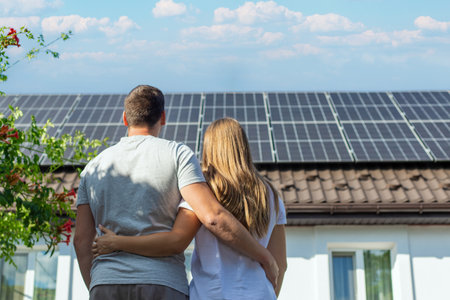 Young couple embracing, looking at solar panels on the roof of their house.の写真素材