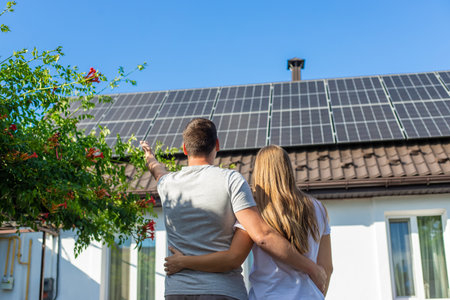Young couple embracing, looking at solar panels on the roof of their house.の写真素材