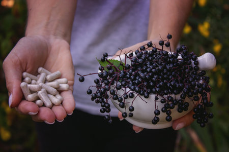 Woman's hands holding elderberry: berries, syrup and capsules. Healthy nutritionの写真素材