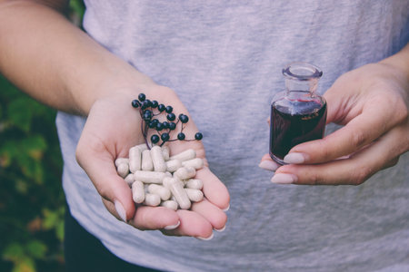 Woman's hands holding elderberry: berries, syrup and capsules. Healthy nutritionの写真素材