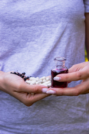 Woman's hands holding elderberry: berries, syrup and capsules. Healthy nutritionの写真素材