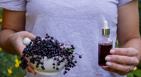 Woman's hands holding elderberry: berries, syrup and capsules. Healthy nutrition