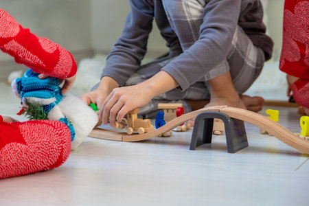 Three children playing with a wooden toy train set near the Christmas tree at home.の写真素材