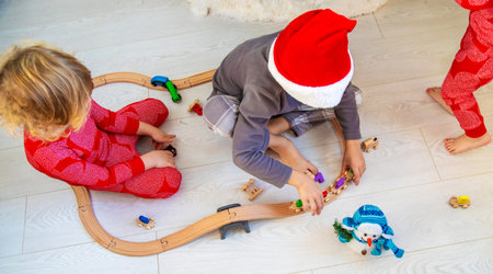 A boy and a girl are playing with a wooden toy train near a Christmas tree at home