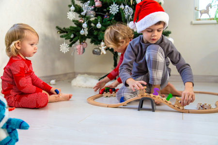 Three children playing with a wooden toy train set near the Christmas tree at home.の写真素材