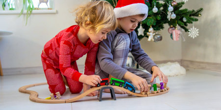 A boy and a girl are playing with a wooden toy train near a Christmas tree at home