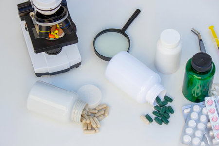 Microscope, medicine bottles, and magnifying glass on a white table for medical research.の写真素材