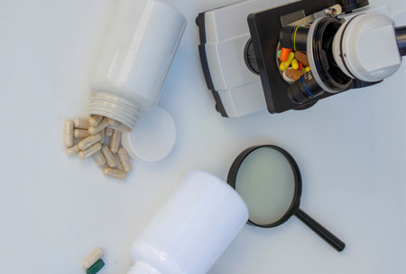 Microscope, medicine bottles, and magnifying glass on a white table for medical research.の写真素材