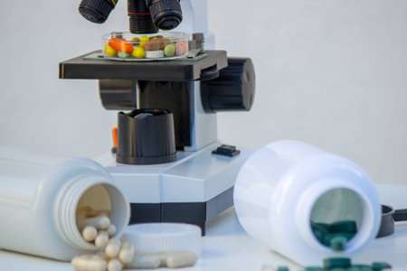 Microscope, medicine bottles, and magnifying glass on a white table for medical research.