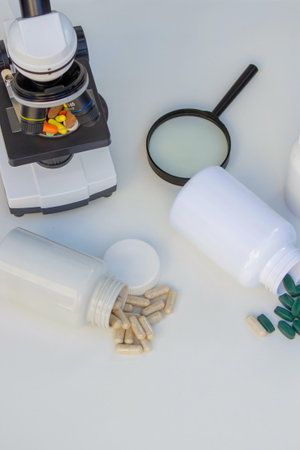 Microscope, medicine bottles, and magnifying glass on a white table for medical research.の写真素材