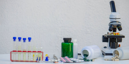 Microscope, medicine bottles, and magnifying glass on a white table for medical research.の写真素材