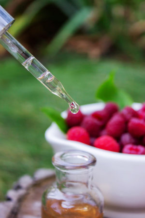 Fresh raspberries in a mortar with a bottle of natural herbal extract or essential oil outdoorsの写真素材