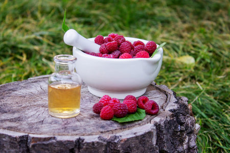 Fresh raspberries in a mortar with a bottle of natural herbal extract or essential oil outdoorsの写真素材