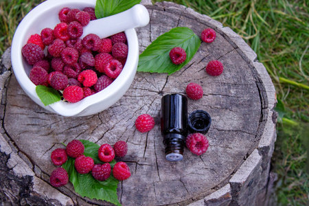 Fresh raspberries in a mortar with a bottle of natural herbal extract or essential oil outdoors