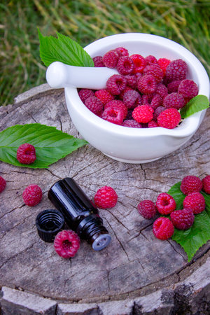 Fresh raspberries in a mortar with a bottle of natural herbal extract or essential oil outdoorsの写真素材