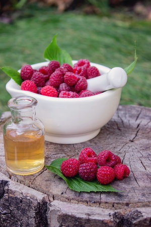 Fresh raspberries in a mortar with a bottle of natural herbal extract or essential oil outdoorsの写真素材