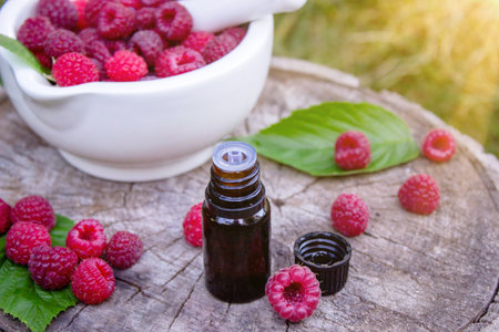 Fresh raspberries in a mortar with a bottle of natural herbal extract or essential oil outdoorsの写真素材