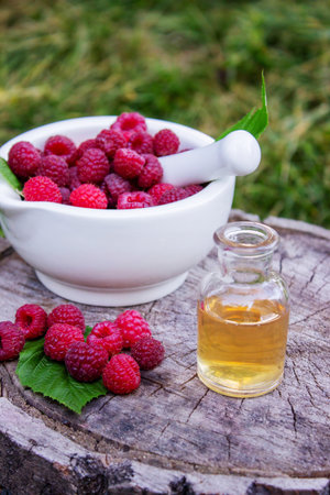 Fresh raspberries in a mortar with a bottle of natural herbal extract or essential oil outdoorsの写真素材