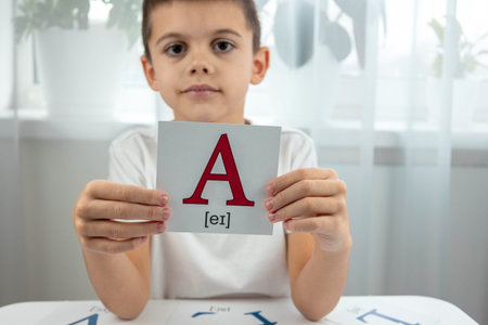 Boy holding a flashcard with the capital letter A and its phonetic transcription.の写真素材