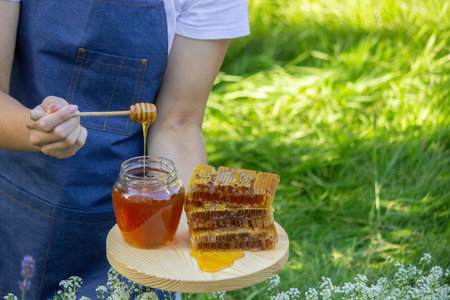Natural honey dripping from a wooden dipper into a glass jar against a floral background.