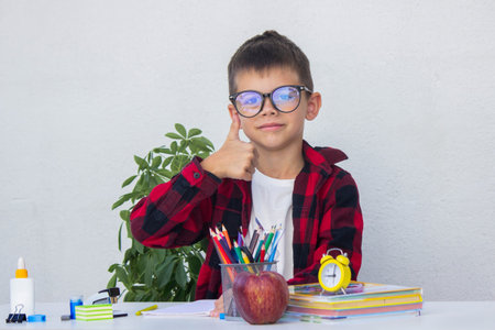 Smart young boy in glasses preparing for school, choosing pencils from the organizer on his desk