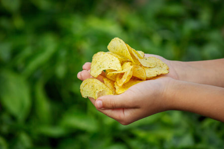 Child's hands holding a handful of crispy, seasoned potato chips against a green background.