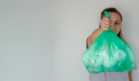 Woman holding a large green trash bag filled with used disposable baby diapers.の写真素材
