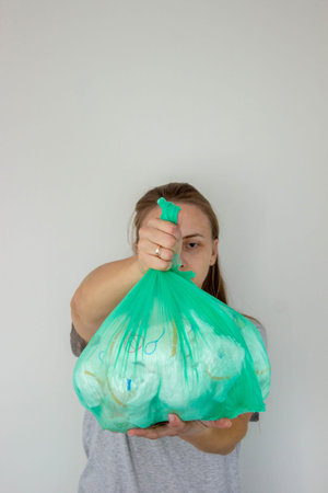 Woman holding a large green trash bag filled with used disposable baby diapers.