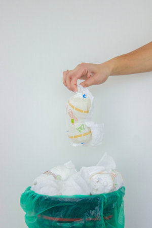 A woman's hand disposing of a used baby diaper into a trash can with a green liner.の写真素材
