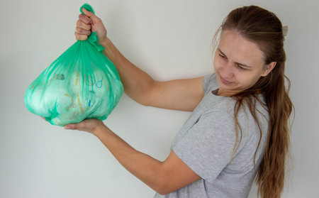 Woman holding a large green trash bag filled with used disposable baby diapers.