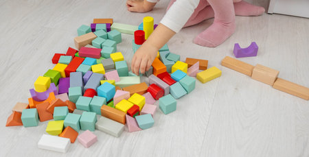 Little girl building a tower with colorful wooden blocks on the floor