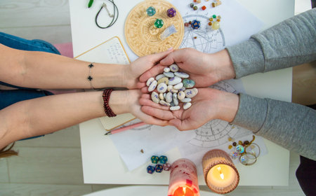 View of two pairs of hands holding rune stones over astrological chart during fortune telling session.の写真素材