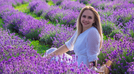 Woman in white dress at picnic in lavender field holding a glass of wine.の写真素材