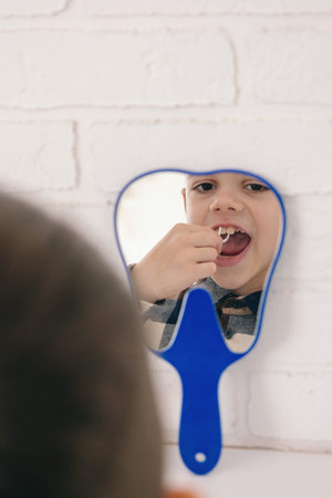 Boy using dental floss pick in mirror.