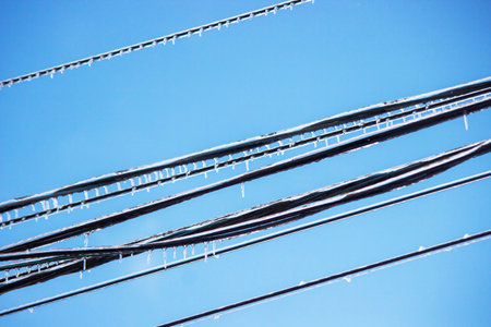 Icy icicles on electric wires against blue sky, freezing rain consequencesの写真素材